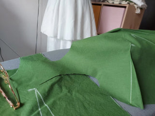 Work in progress: green handmade dress being assembled by Corina, featuring chalk pattern lines and sewing tools at her studio in Iași, Romania.