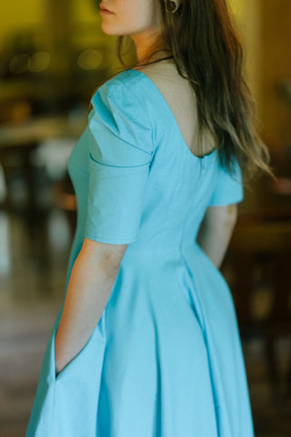 Close-up of the Bubbles Dress by Cori Tailor — showcasing puff sleeve, scoop back, and soft pleats in light blue cotton fabric

