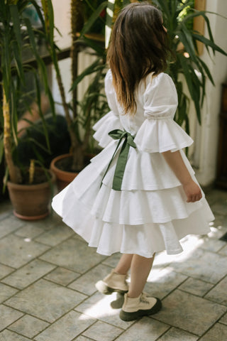 Model twirling in the Freya Dress by Cori Tailor, back view with puff sleeves, layered skirt in motion, and green bow sash