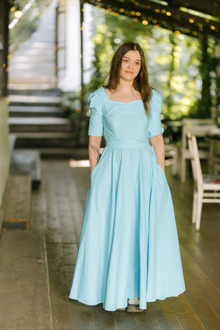Model wearing the Jasmine Set — sweetheart neckline crop top and full circle maxi skirt in turquoise cotton — photographed in an outdoor terrace setting.