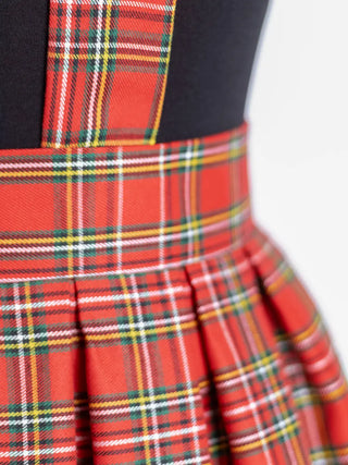 Close-up of the Jenny Skirt showing red tartan fabric, crisp box pleats, and suspender strap attachment – handmade with classic schoolgirl charm by Cori Tailor.